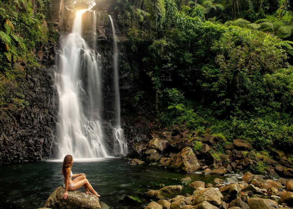 Young woman sitting by Middle Tavoro Waterfalls in Bouma National Heritage Park on Taveuni Island, Fiji